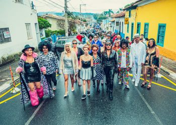 Personagens caracterizados em rua lateral e muitas pessoas ao fundo